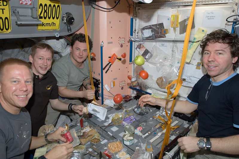 Crew members sharing a meal at the galley on the International Space Station.