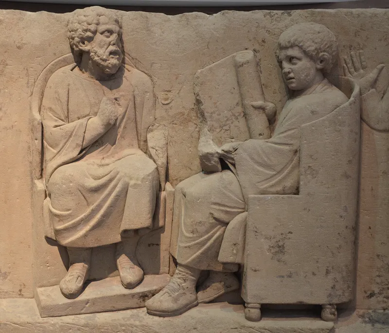 A carved relief from Neumagen, Germany, showing a teacher with pupils holding scrolls and a writing tablet.